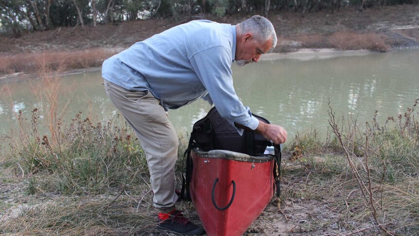 A grey haired man prepares his canoe on the banks of a river.