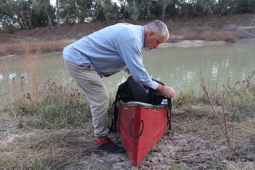 A grey haired man prepares his canoe on the banks of a river.