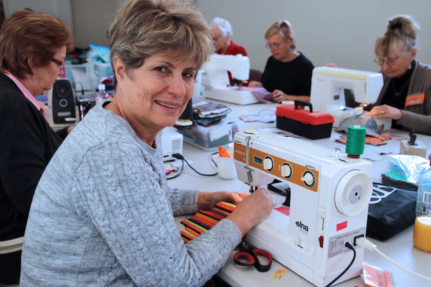 A woman working on a sewing machine... others in the background also toil away at machines.