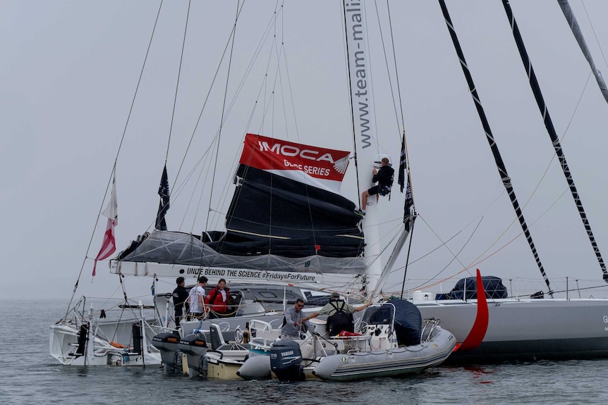 A silver sailboat with Unite behind Science hashtag Fridays For Future prepares to offload crew on a tugboat