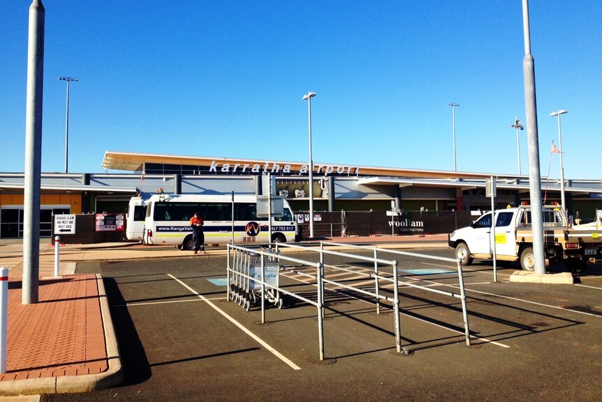 The front facade of Karratha Airport with vehicles parked in the foreground.
