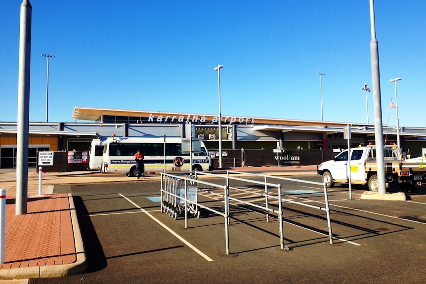 The front facade of Karratha Airport with vehicles parked in the foreground.