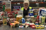 A woman stands around a table full of donated food. 