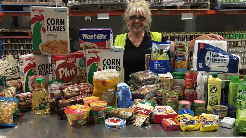 A woman stands around a table full of donated food. 