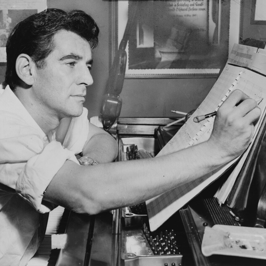 Leonard Bernstein marking up a score while seated at a piano.