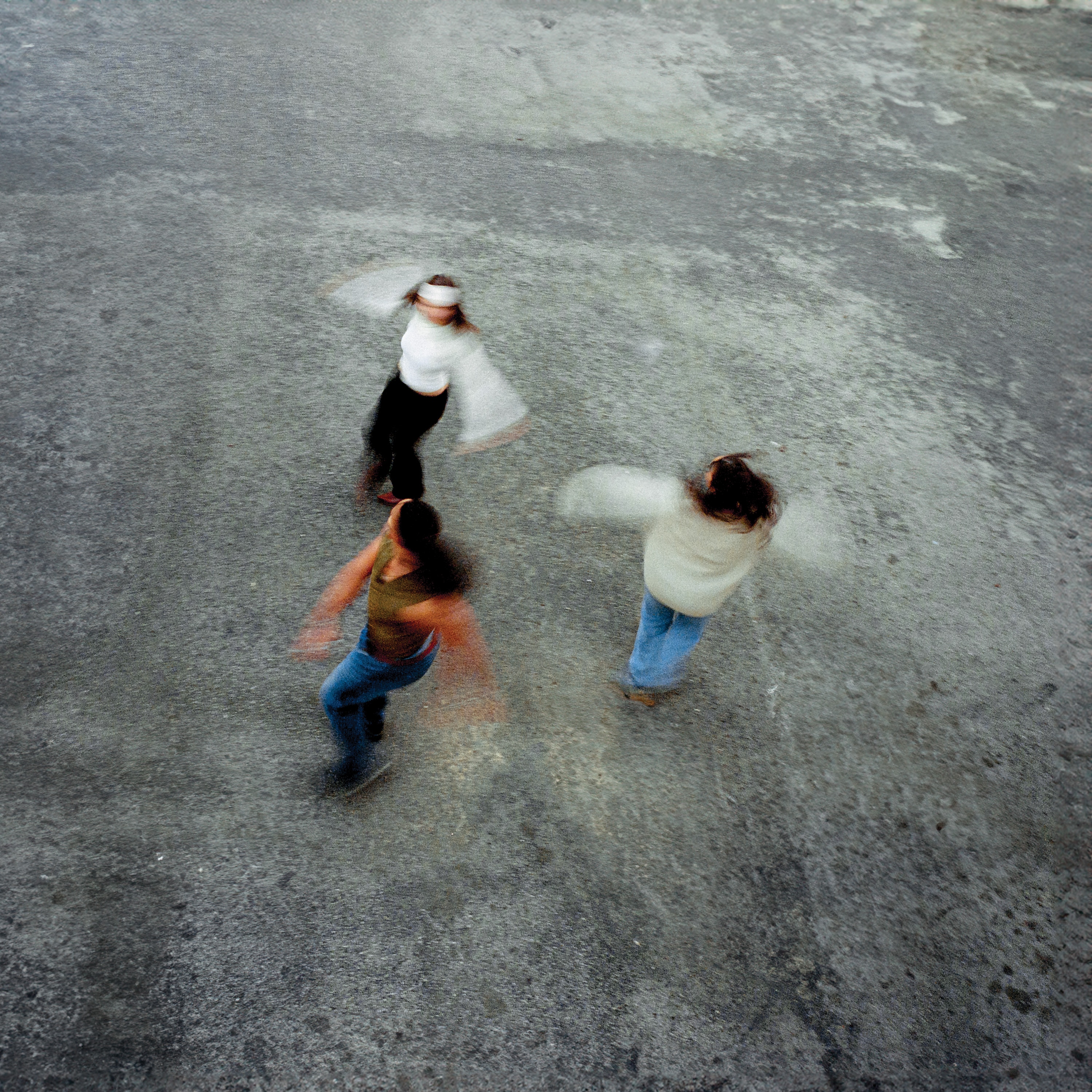 Birds eye view of Boston trio Tiny Hands spinning in blurred motion on grey tarmac