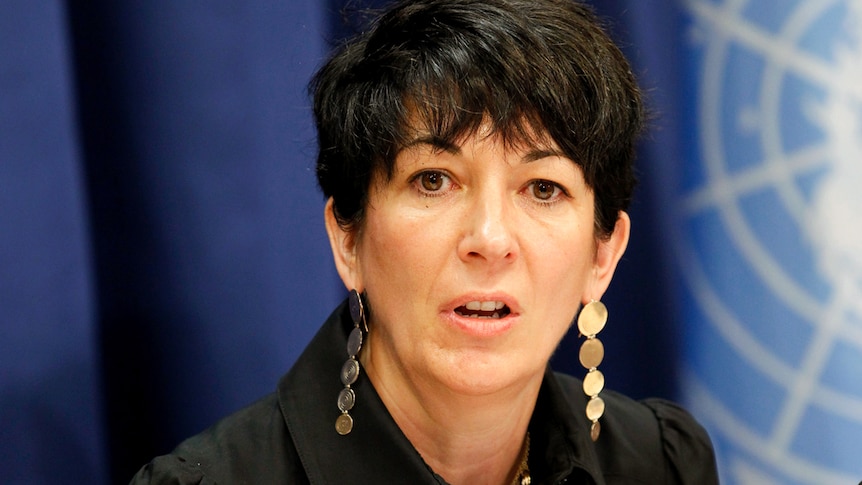 Ghislaine Maxwell wearing long earrings talks in front of a blue background.