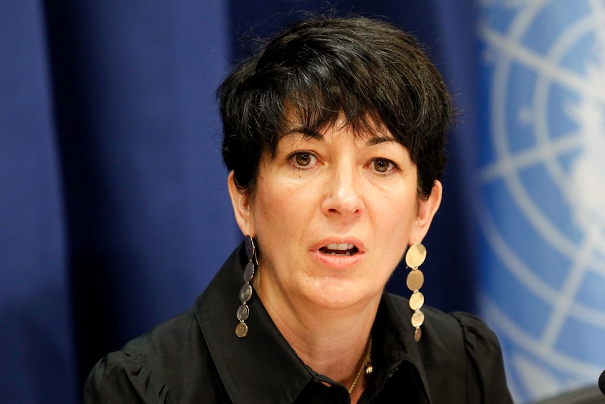 Ghislaine Maxwell wearing long earrings talks in front of a blue background.