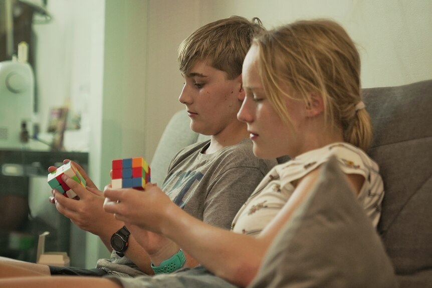 Two teenagers sit on a couch holding Rubik's cubes.