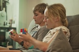 Two teenagers sit on a couch holding Rubik's cubes.