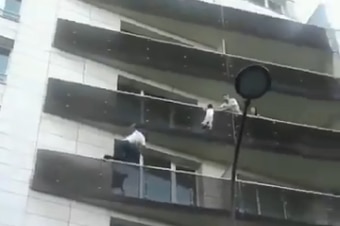 A man is scaling a residential apartment building to save a young boy who is hanging from a balcony on the fourth storey.