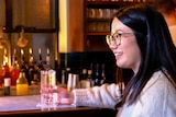 A young woman is sitting in a wine bar holding a glass of soda water as she chats with a young man.  