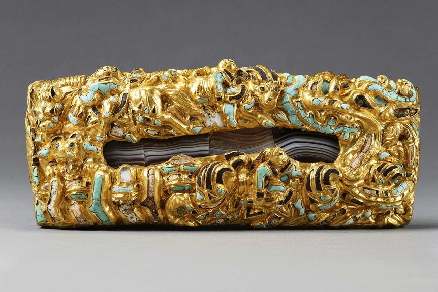 A close up of an elaborate gold, agate, jade and turquoise belt plaque.