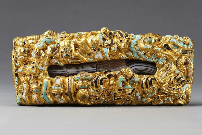 A close up of an elaborate gold, agate, jade and turquoise belt plaque.