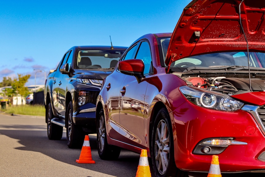 Red car with bonnet up and orange cones