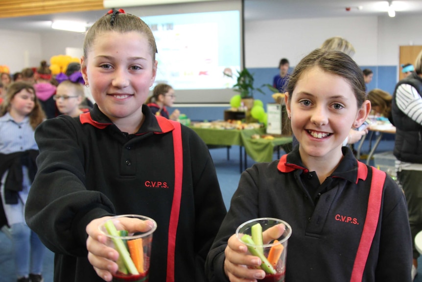 Two young girls holding cups of carrot and celery