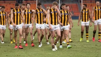 A group of AFL players walk off looking glum after losing a match.