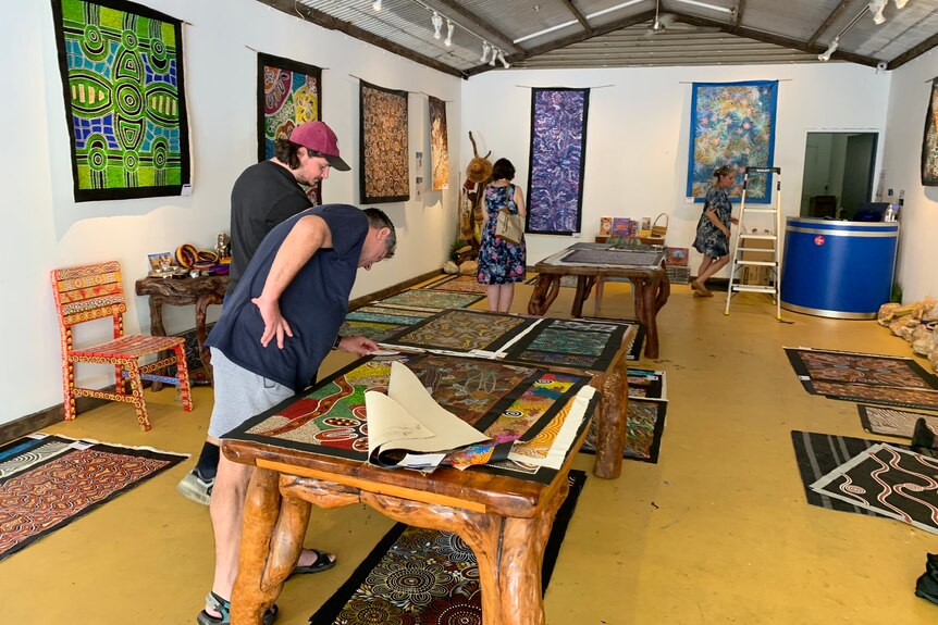 Tourists looking at paintings on a table at a Darwin art gallery.