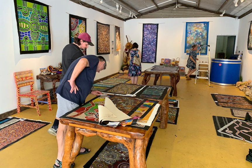 Tourists looking at paintings on a table at a Darwin art gallery.