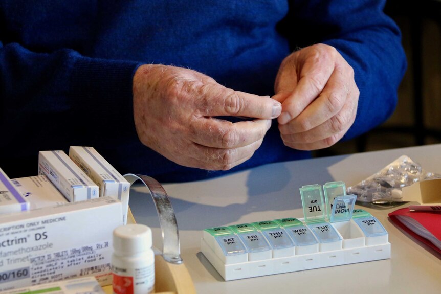 Man wearing a blue jumper handling the medication he has to take.