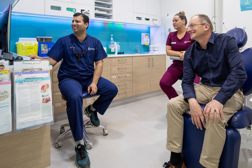 A dentist, a dental nurse and a patient look at a screen during an appointment