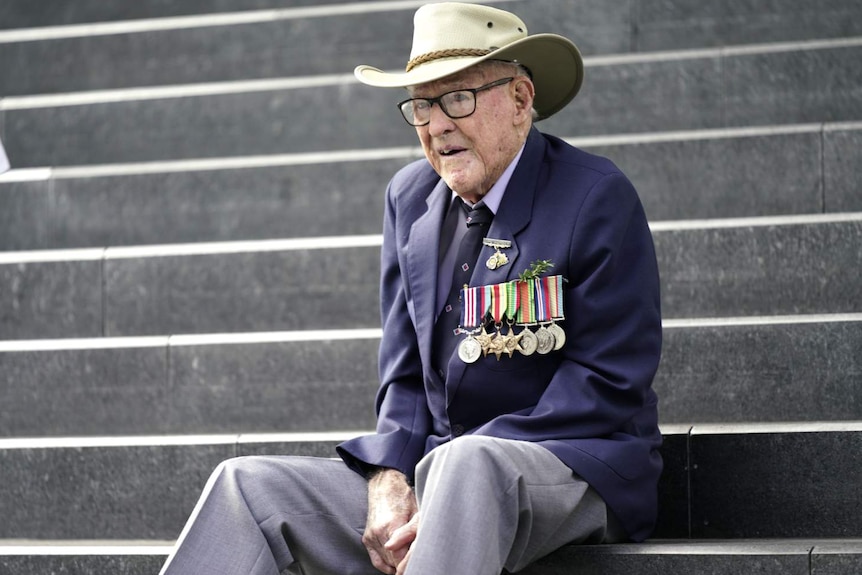 elderly man in hat sitting on stairs with hands clasped