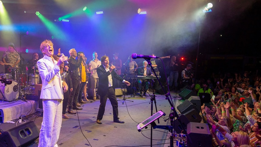 Performers sing on stage at the Fire Aid concert in Bowral in front of a crowd at night.