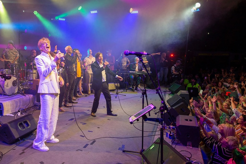 Performers sing on stage at the Fire Aid concert in Bowral in front of a crowd at night.