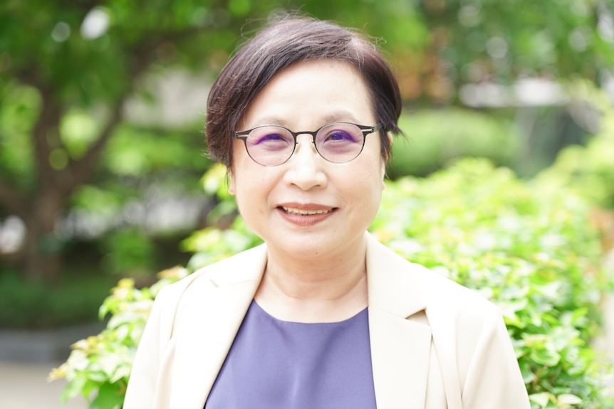 A close up of a woman with dark hair and eyes wearing glasses and smiling