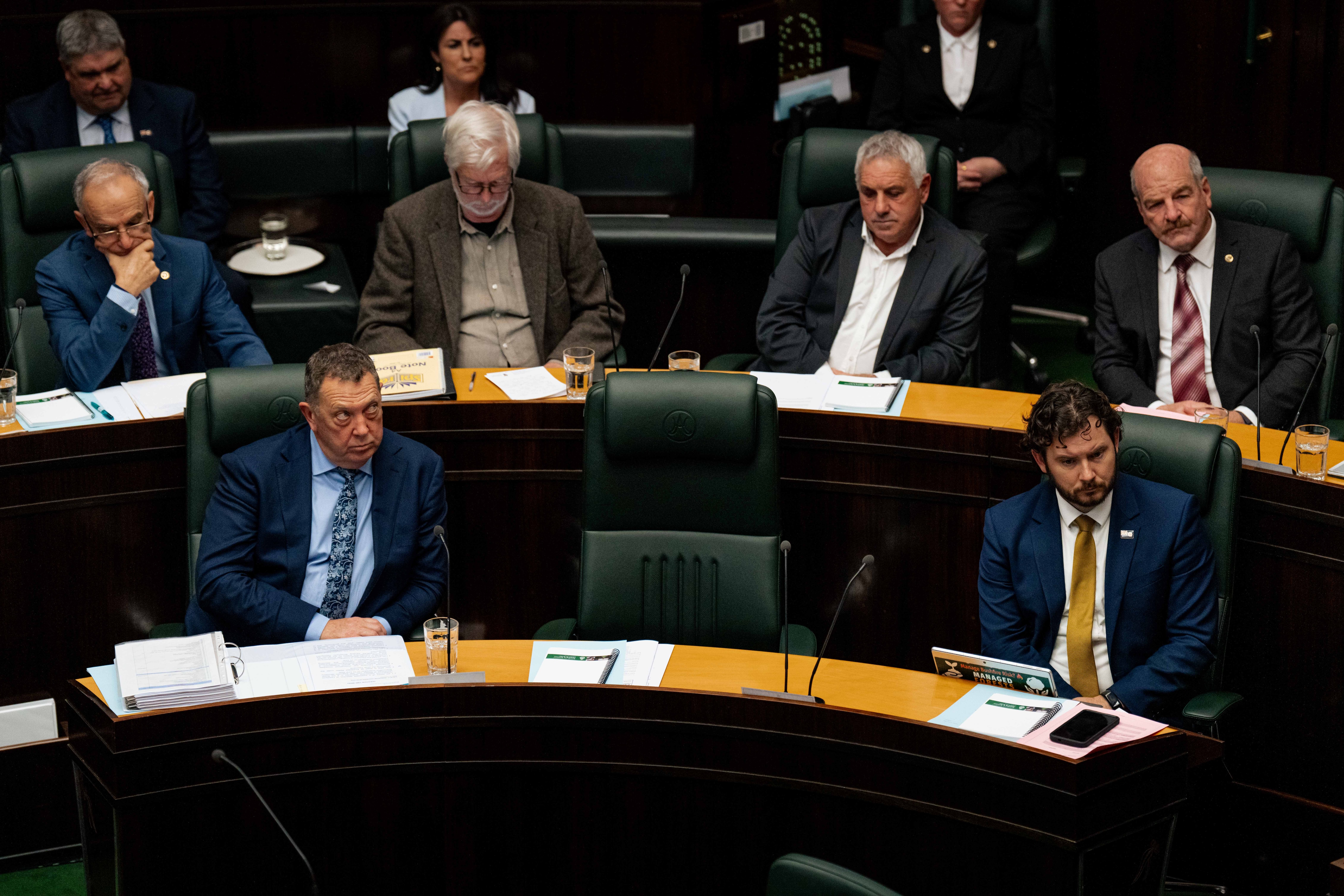 Politicians sit in green chairs, one is empty