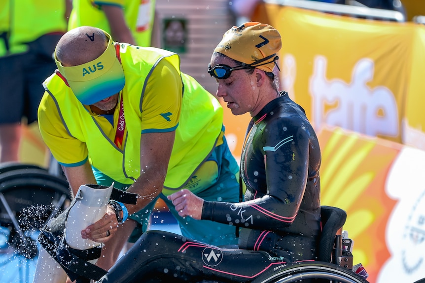 homme avec un chapeau australien aidant une athlète féminine à changer de combinaison de plongée