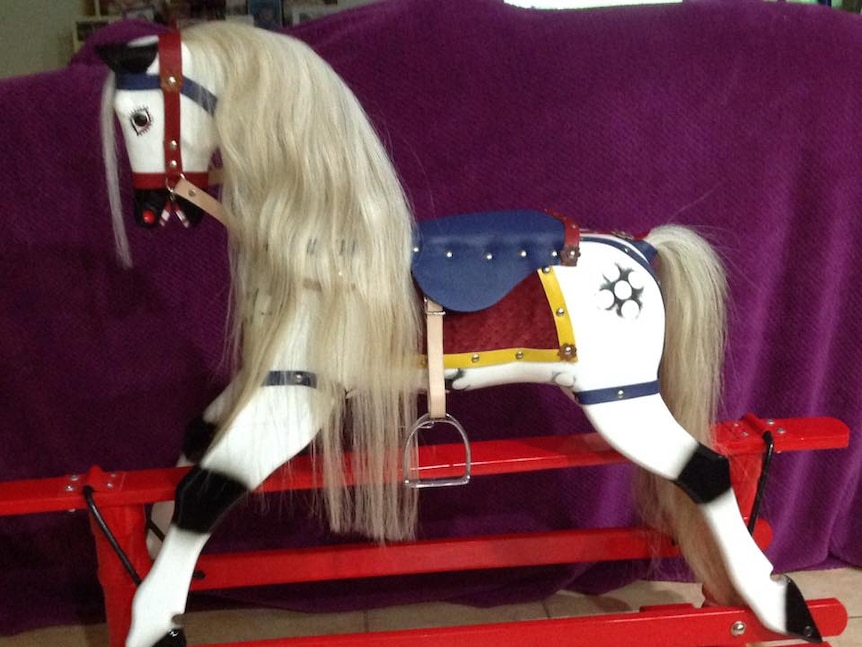 A newly painted white rocking horse, with a long flowing white main, blue saddle and black finishings.