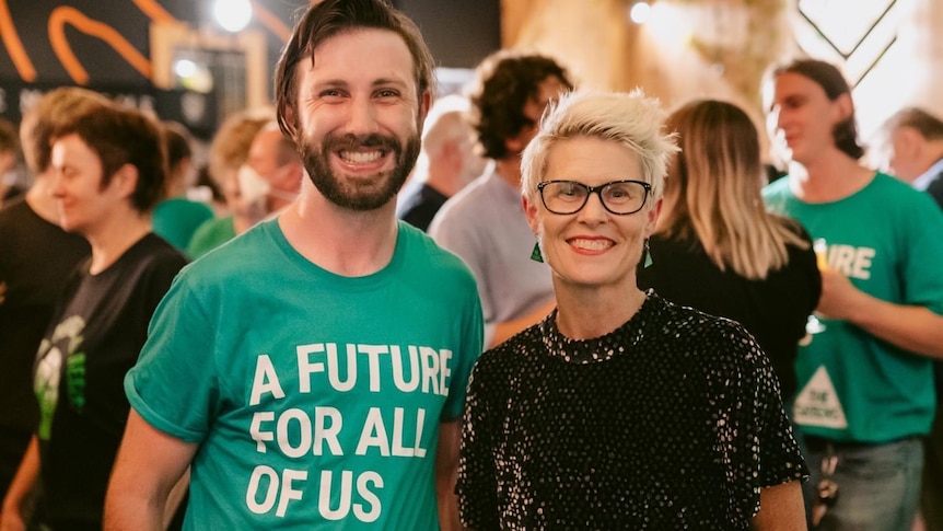A man in a Greens tshirt and a woman smile at the camera