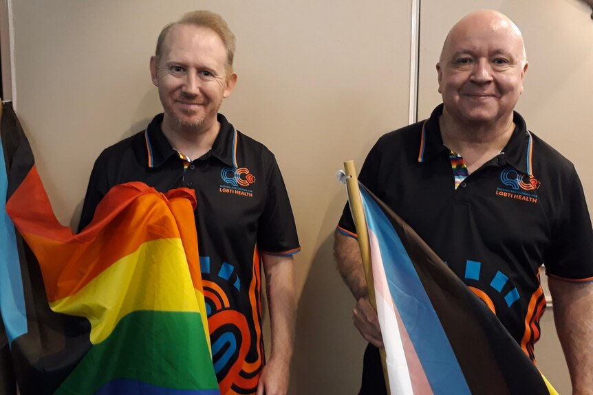 Two men stand holding rainbow and transgender flags.