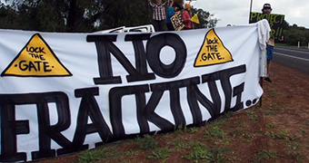 Protesters stand next to a large banner with No Fracking painted on it.