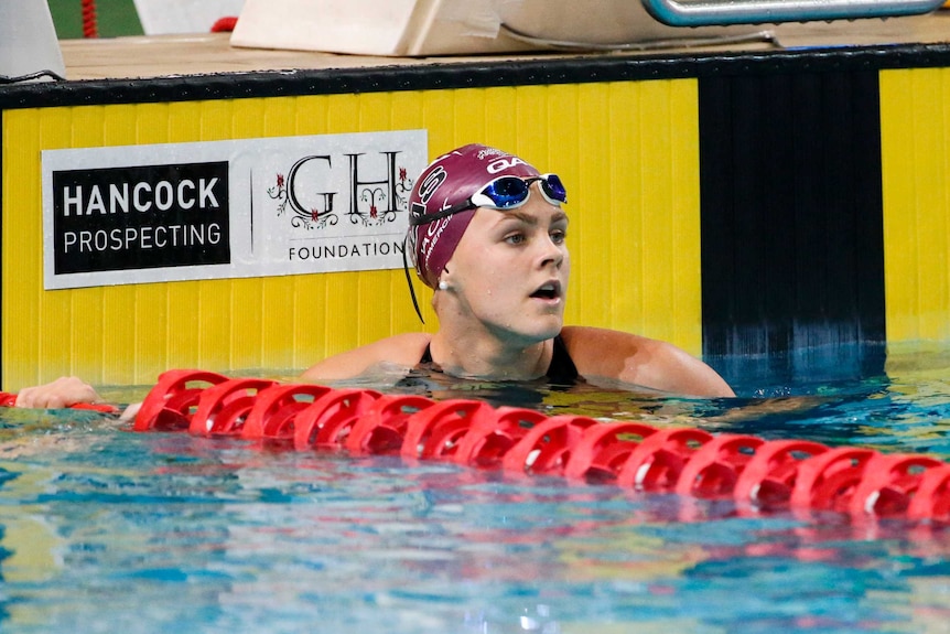 A female swimmer at the finish wall looking at the scoreboard.