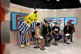 A television set with four seated people talking. Behind them are six dressed up characters, including the Bananas in Pyjamas.