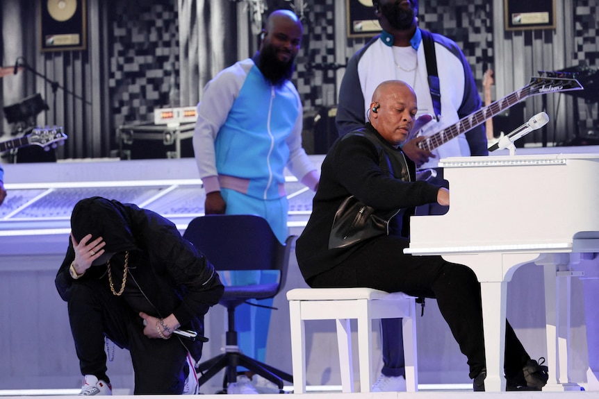 Dr Dre at piano while Eminem takes a knee