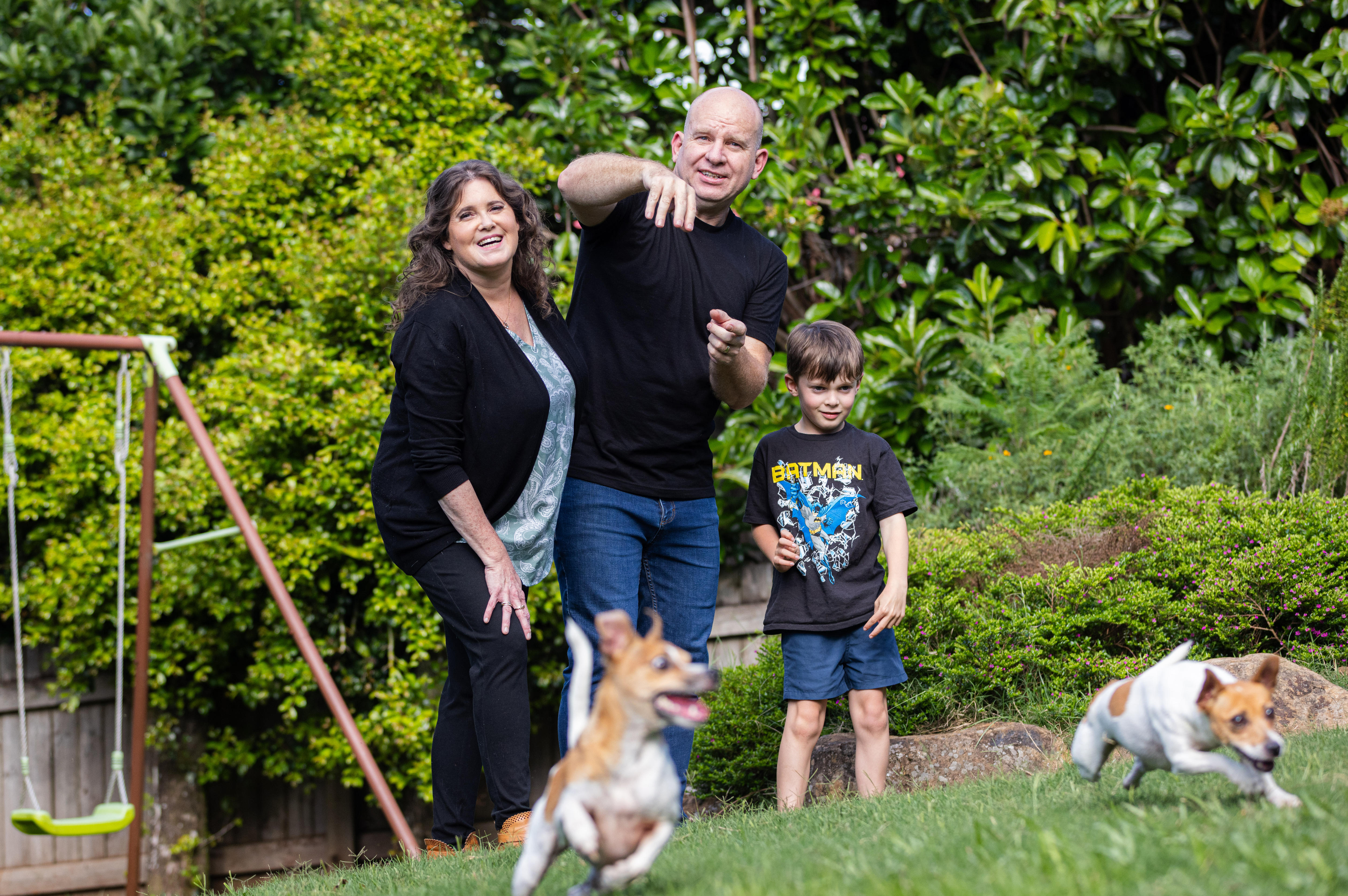A man, woman, and boy smiling at the camera and watching dogs play