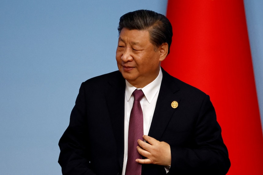 Xi Jinping standing in front of a Chinese flag. 