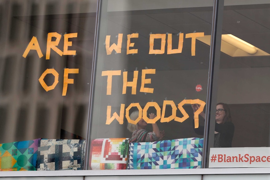 workers stick up post-it notes reading 'are we out of the woods'.