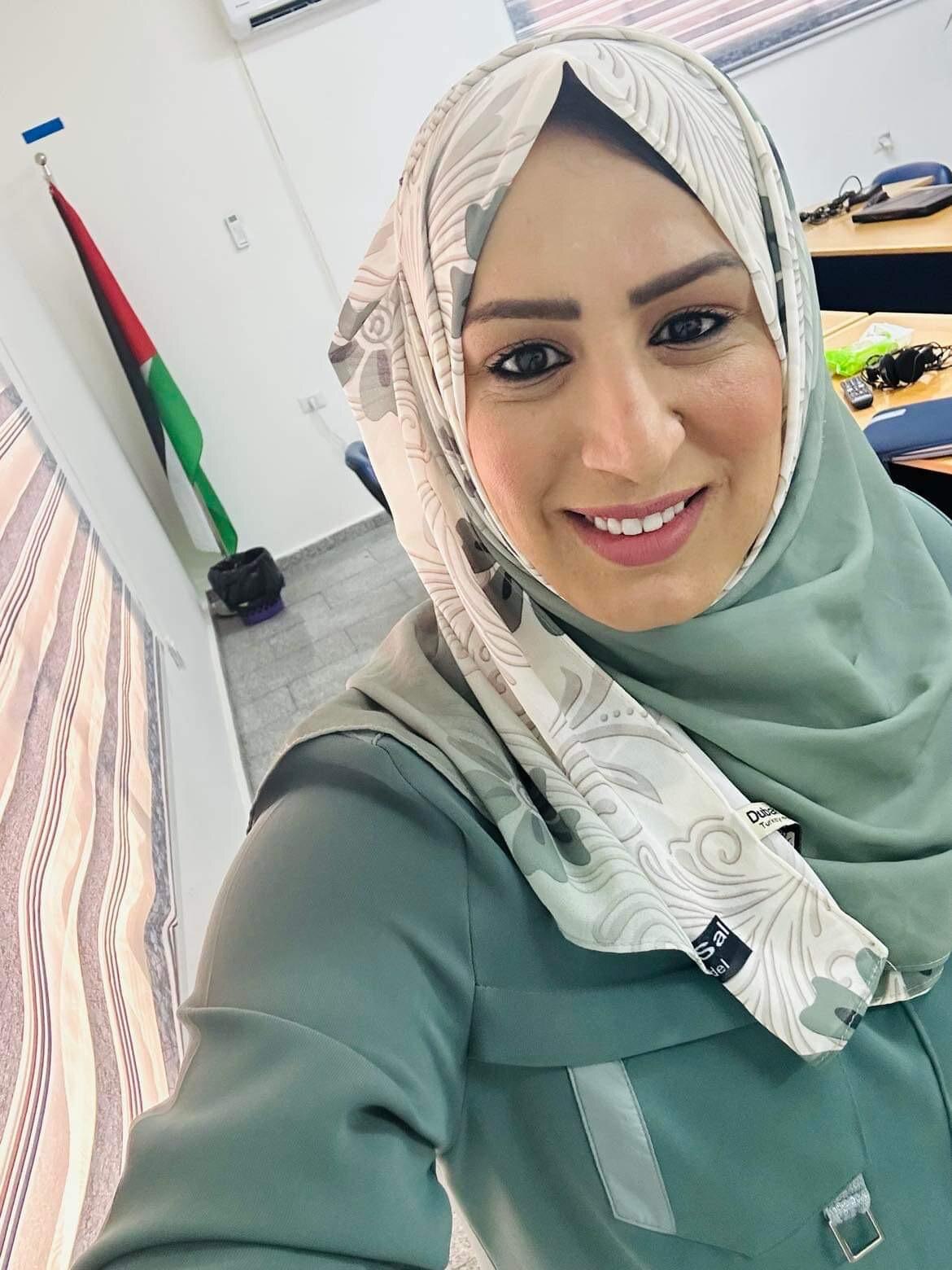 A photo of a woman wearing a beige and grey hijab and green dress. 