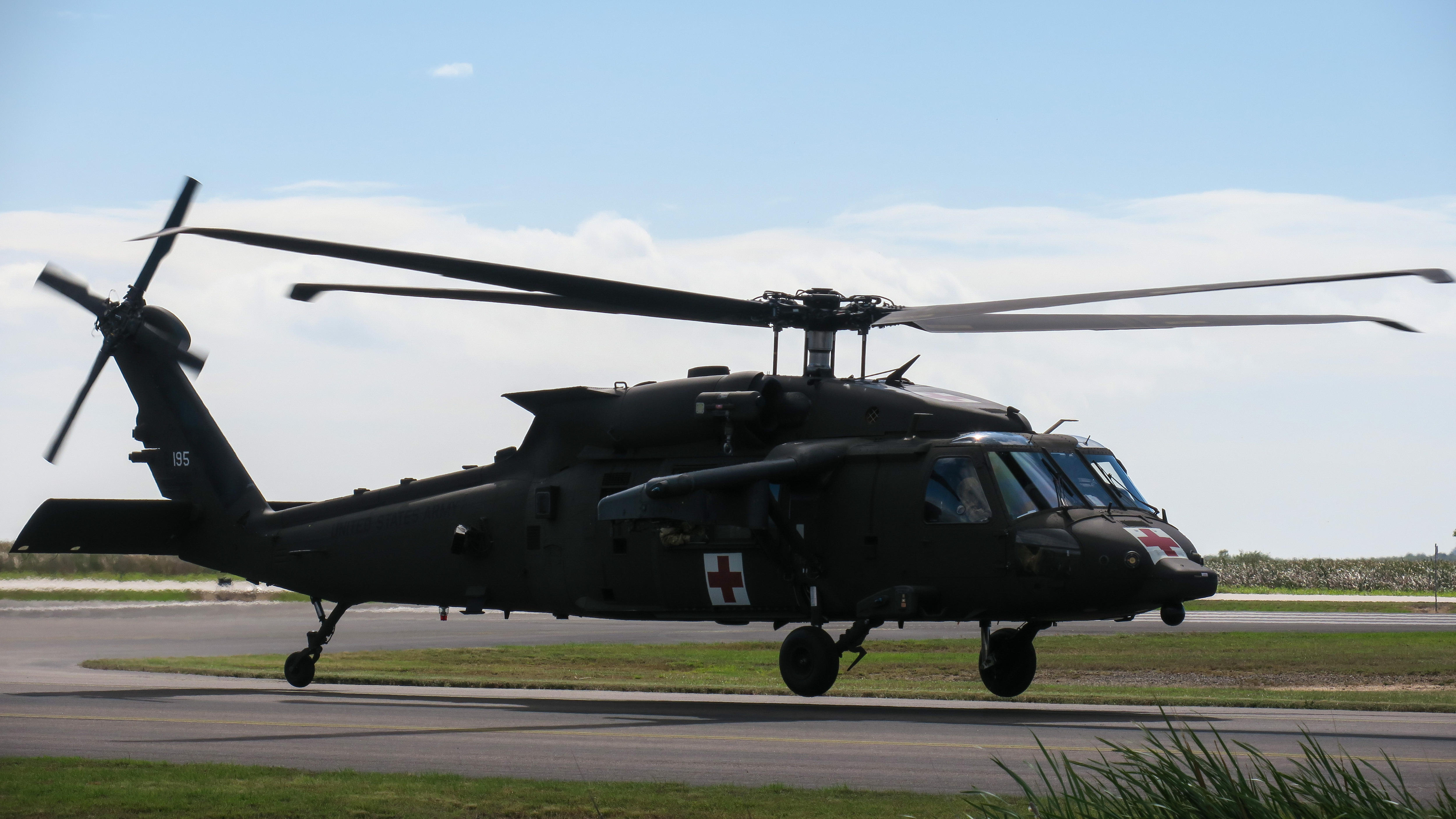 A dark military helicopter hovers a few feet from the airstrip beneath it at the Townsville air base, behind are rolling hills.
