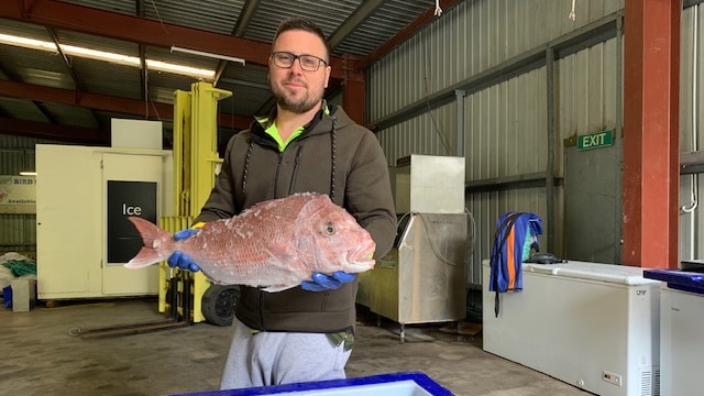 A man holding a fish in a warehouse with freezers