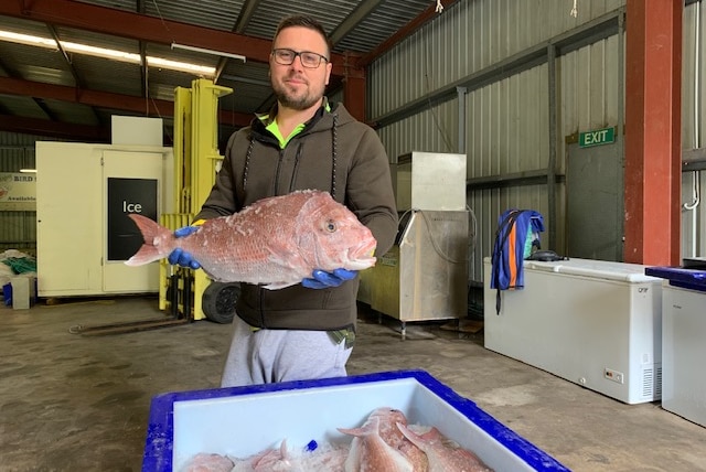 A man holding a fish in a warehouse with freezers