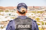 A mid-shot of the back of a female police officer with the town of Mount Isa in the background