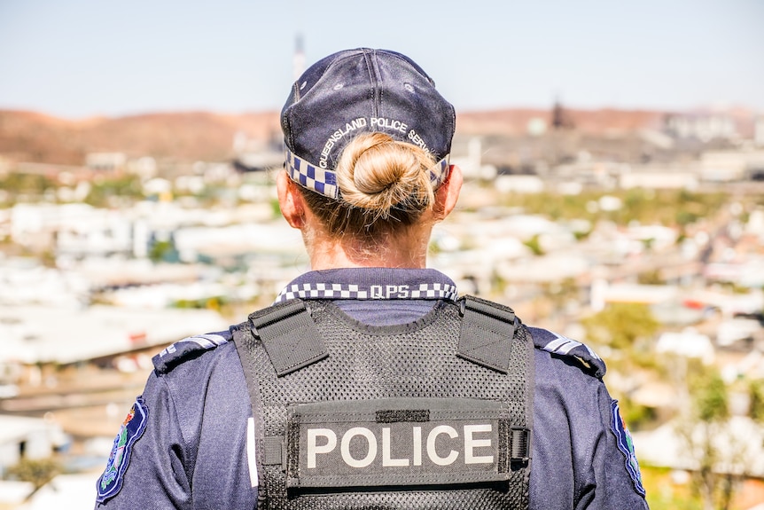 A mid-shot of the back of a female police officer with the town of Mount Isa in the background
