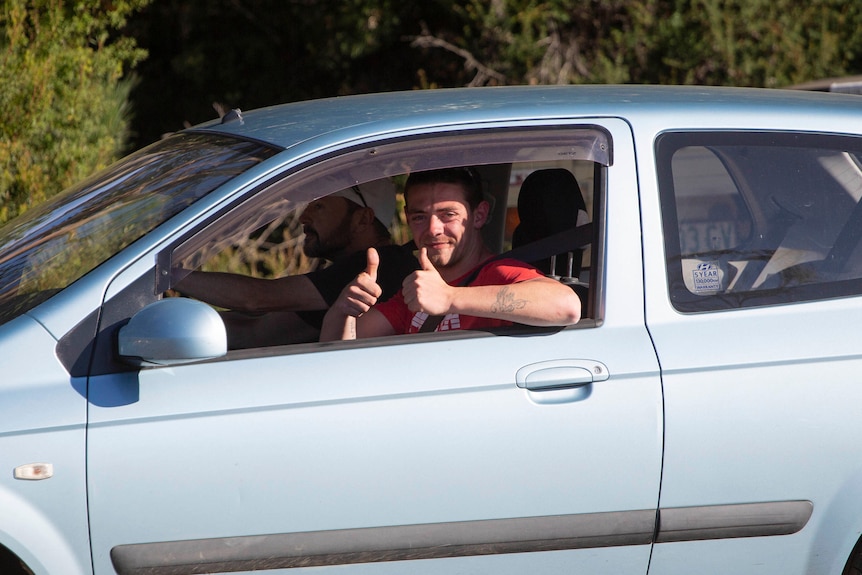 A man in a silver car gives the thumbs up sign