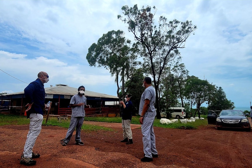 Five people in full PPE speak outside a health clinic in a remote Aboriginal community.