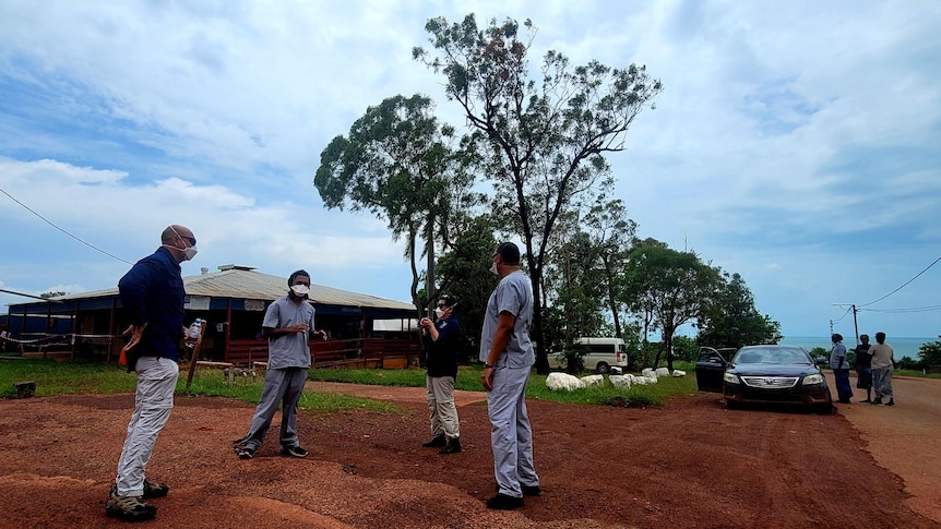 Five people in full PPE speak outside a health clinic in a remote Aboriginal community.